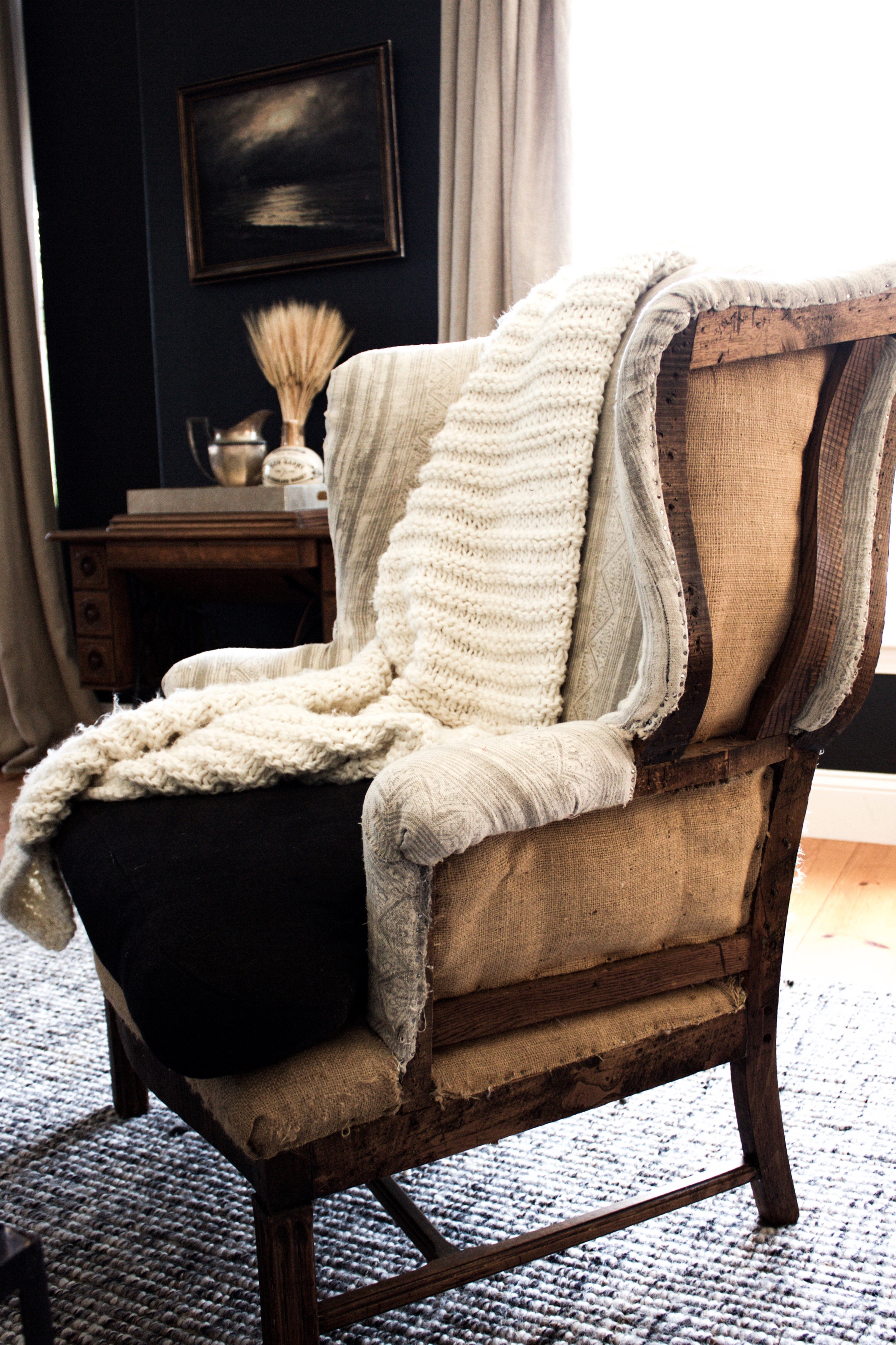 Deconstructed wing back chair with exposed wood frame, black seat cushion, mudcloth, and burlap upholstery